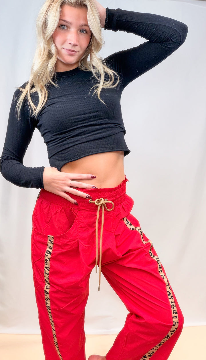 Woman wearing black long sleeve top with red windbreaker pants with cheetah stripes on plain background
