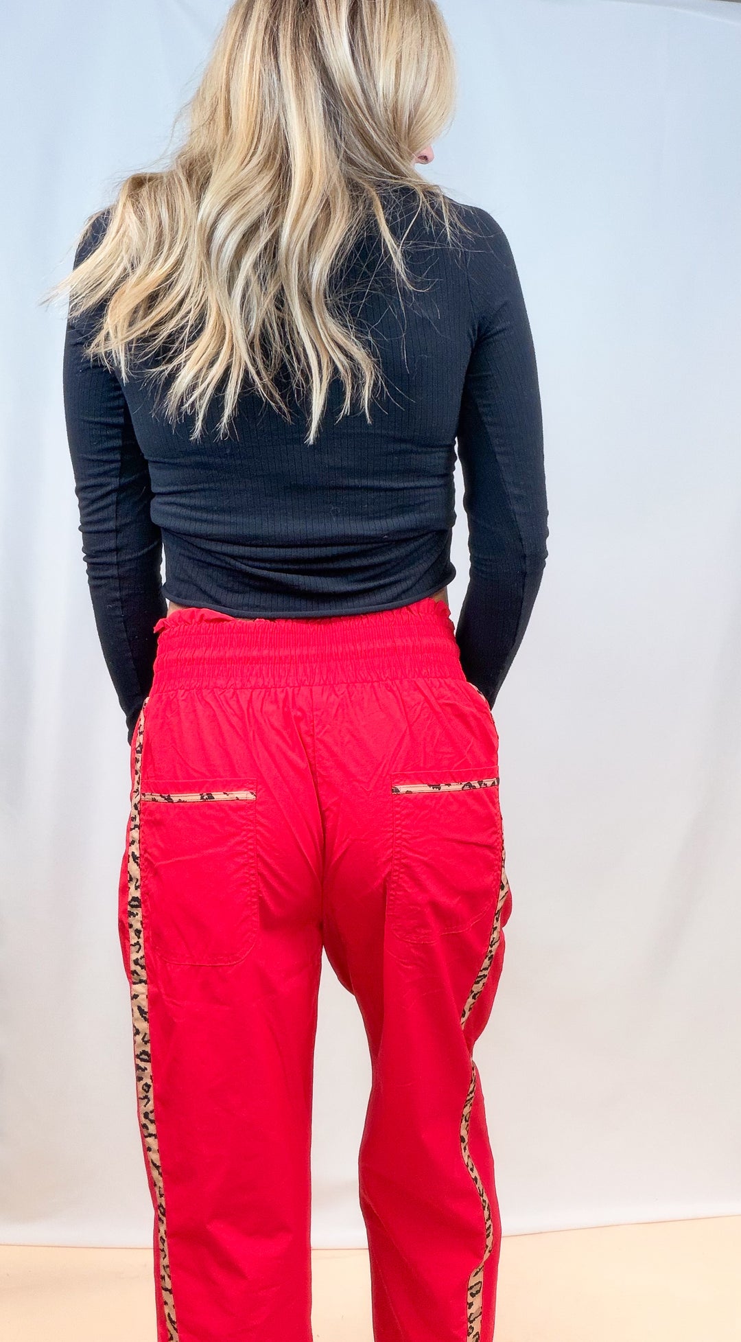 Woman shown from back view wearing black long sleeve top with red windbreaker pants with cheetah details on plain background