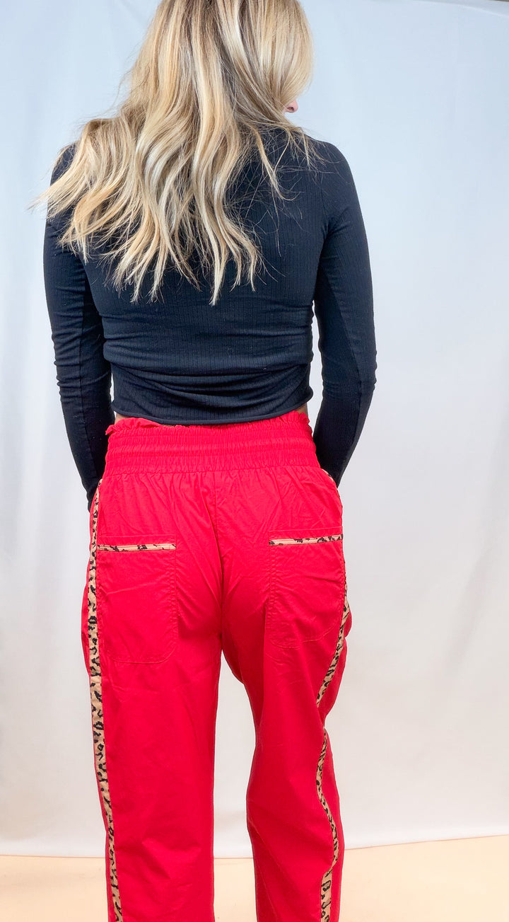 Woman shown from back view wearing black long sleeve top with red windbreaker pants with cheetah details on plain background