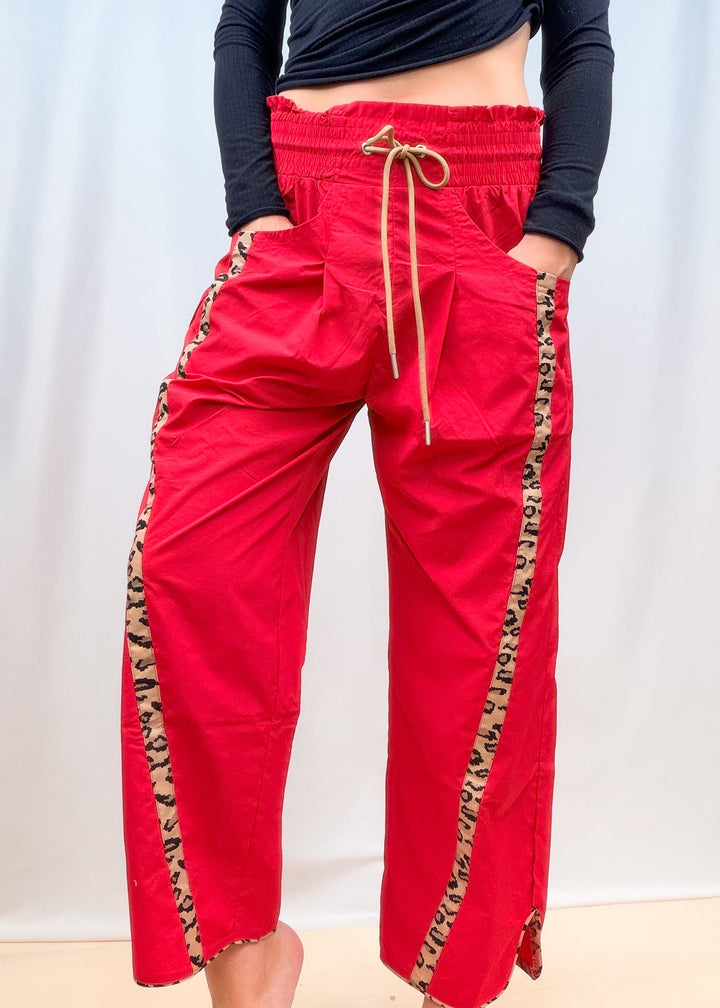 Woman shown waist down wearing black top with red windbreaker pants with cheetah details on plain background