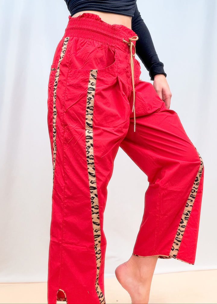 Woman shown from side view wearing black top and red windbreaker pants with cheetah details on plain background