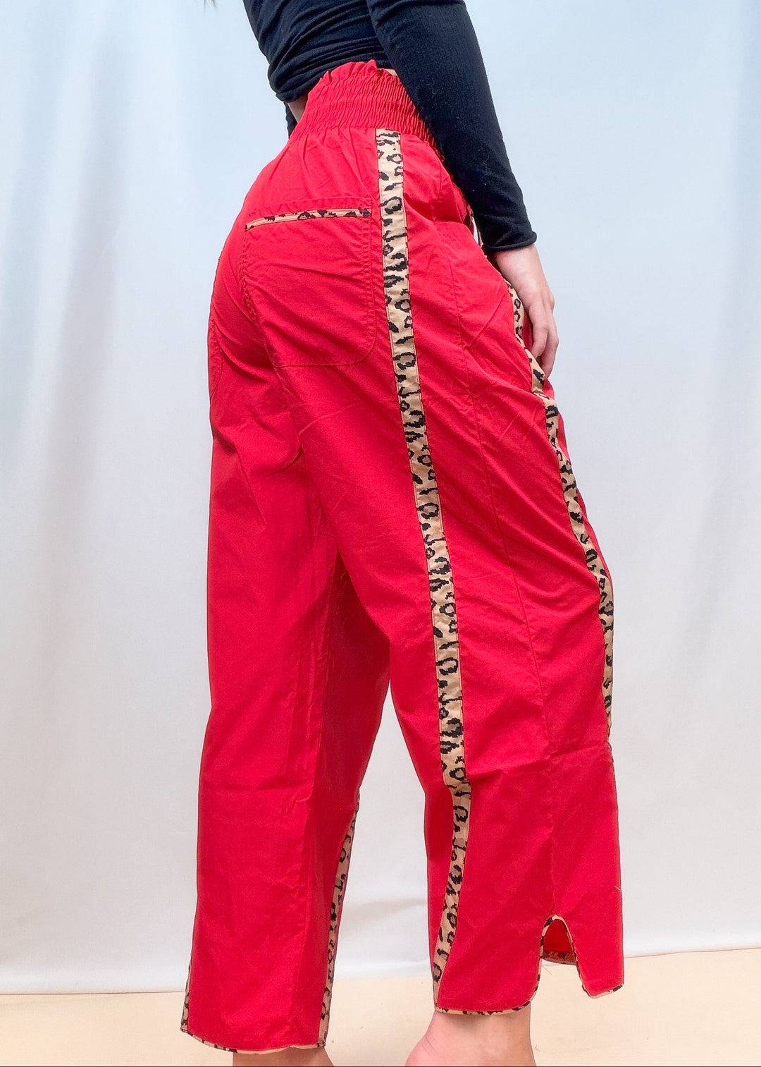 Woman shown from side view wearing black top and red windbreaker pants with cheetah details on plain background