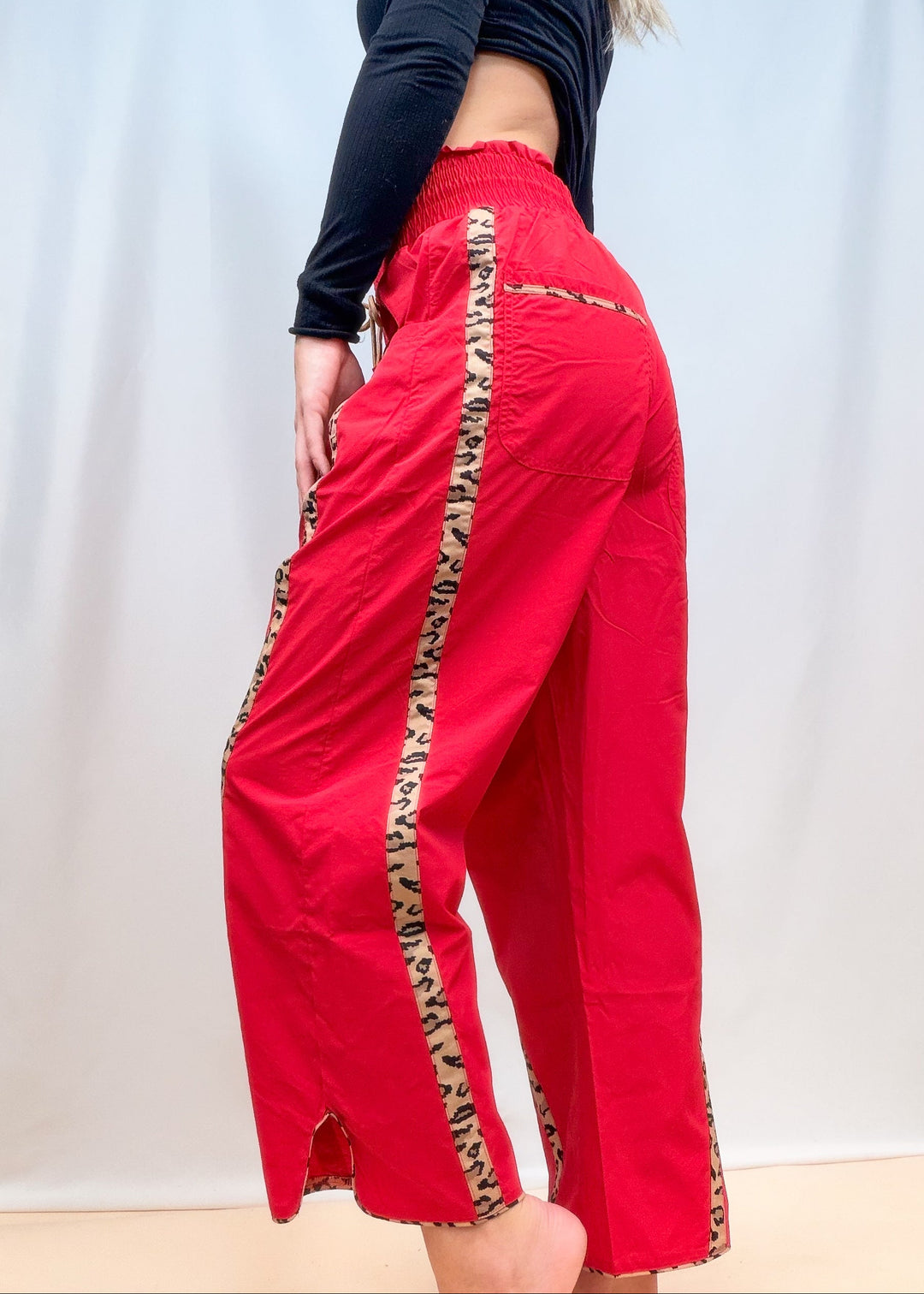 Woman wearing black top with red windbreaker pants with cheetah details on plain background