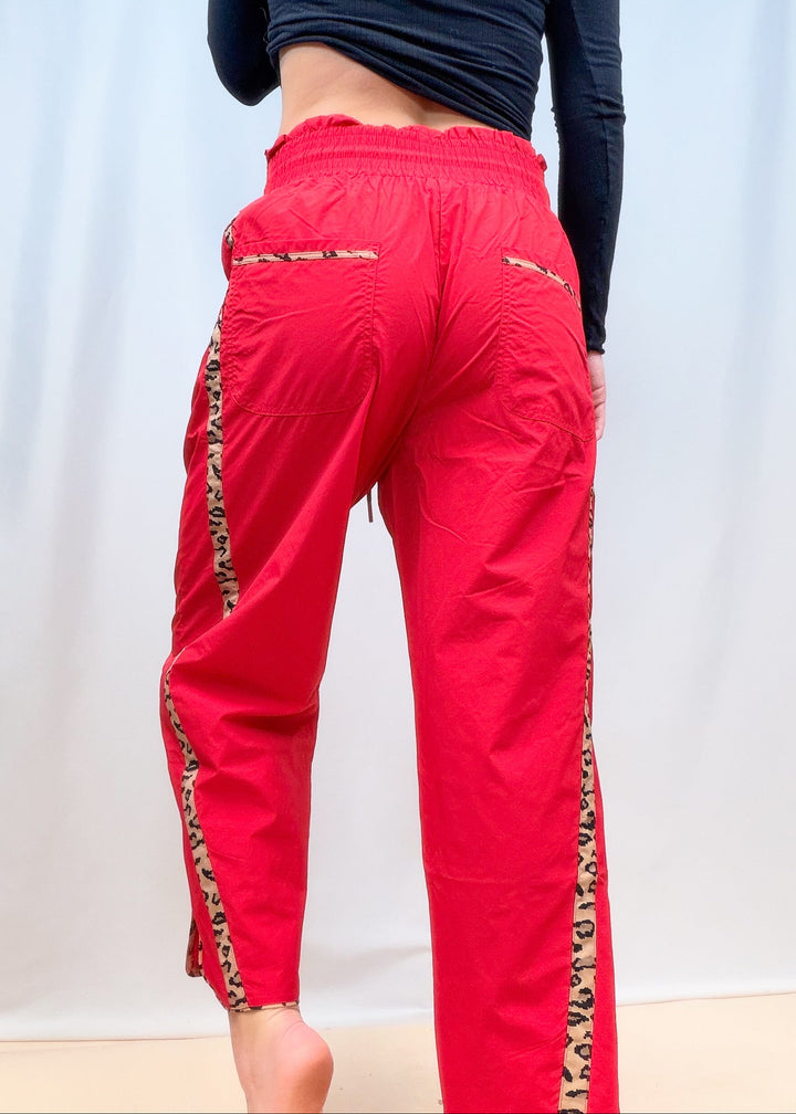 Woman shown from back view wearing red windbreaker pants with cheetah details on plain background