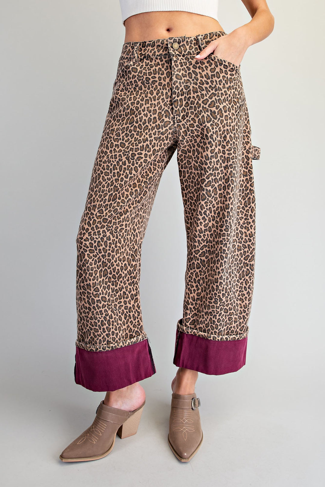 A model wears wide-leg cropped pants featuring a brown and beige leopard print with a contrasting deep magenta ruffle hem, styled with taupe ankle boots against a light gray studio background.
