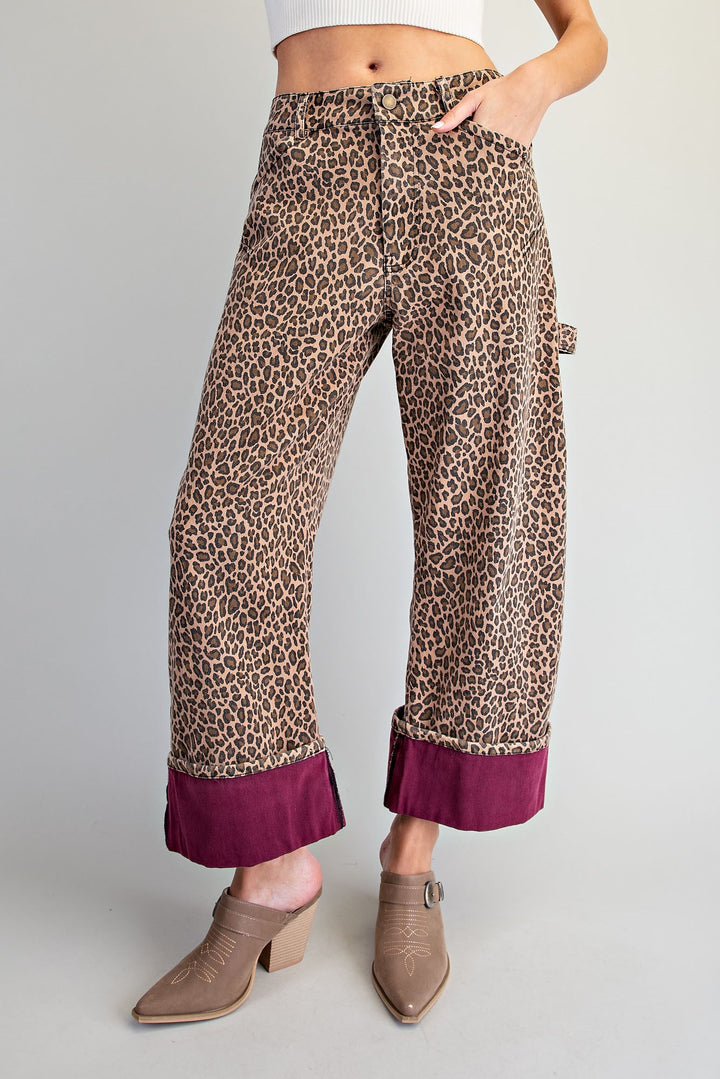 A model wears wide-leg cropped pants featuring a brown and beige leopard print with a contrasting deep magenta ruffle hem, styled with taupe ankle boots against a light gray studio background.