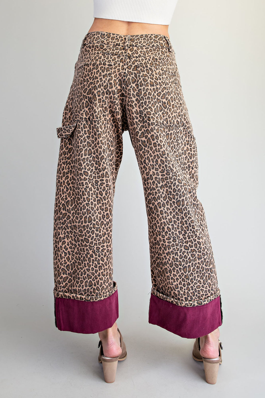 Wide-leg cropped pants with a brown and beige leopard print and a contrasting deep magenta rolled cuff, shown on a model from the back against a light gray background.
