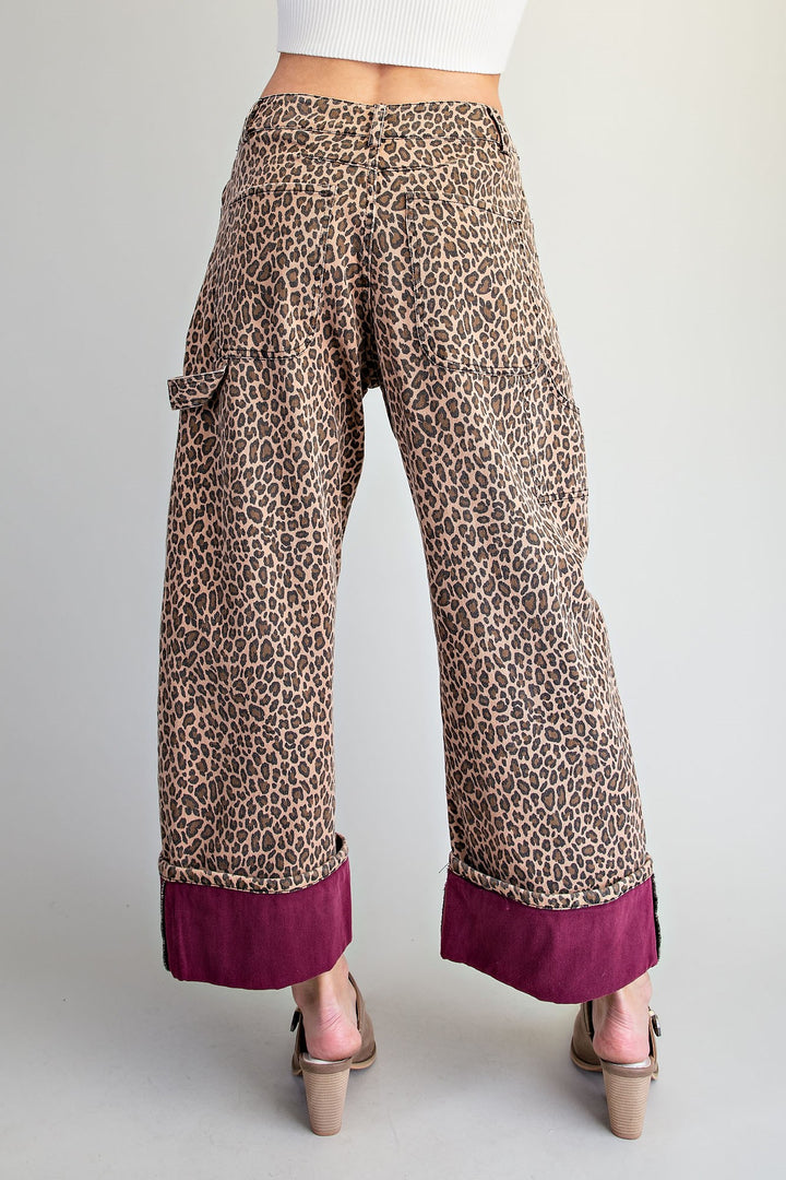 Wide-leg cropped pants with a brown and beige leopard print and a contrasting deep magenta rolled cuff, shown on a model from the back against a light gray background.