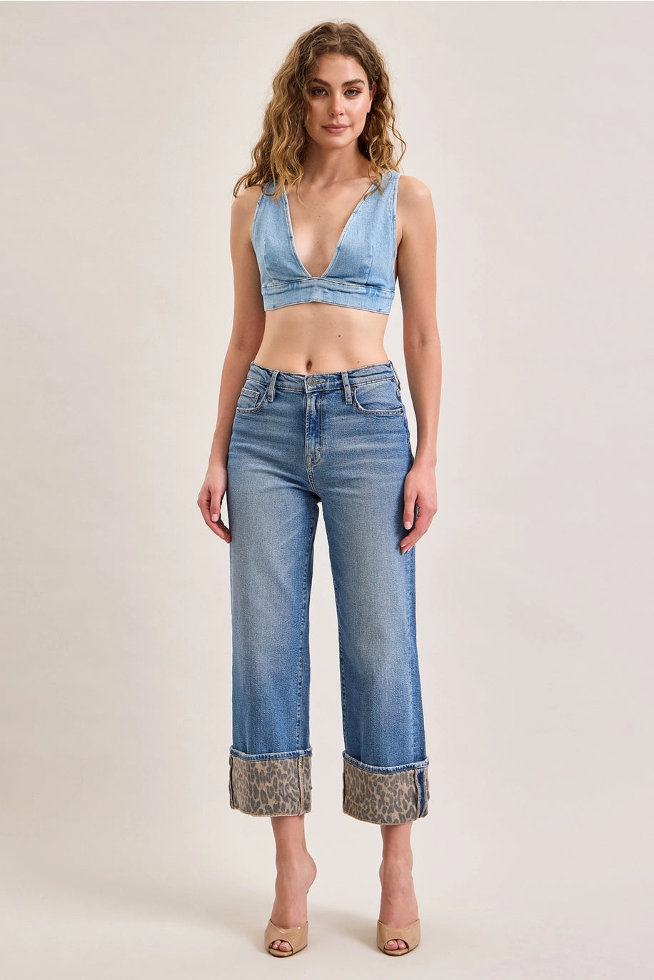 Woman wearing denim pants with leopard cuffs on plain background