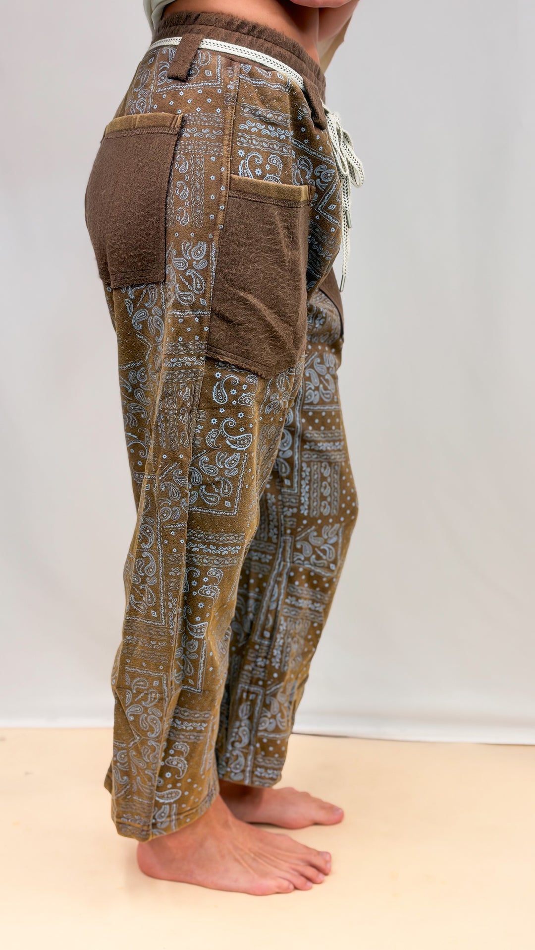 Woman shown from side view wearing brown pants with blue paisley design on plain background