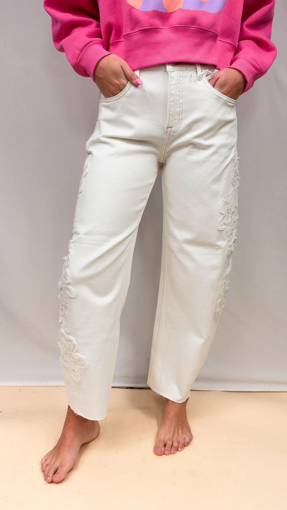 Woman wearing cream colored jeans with flower applique on plain background