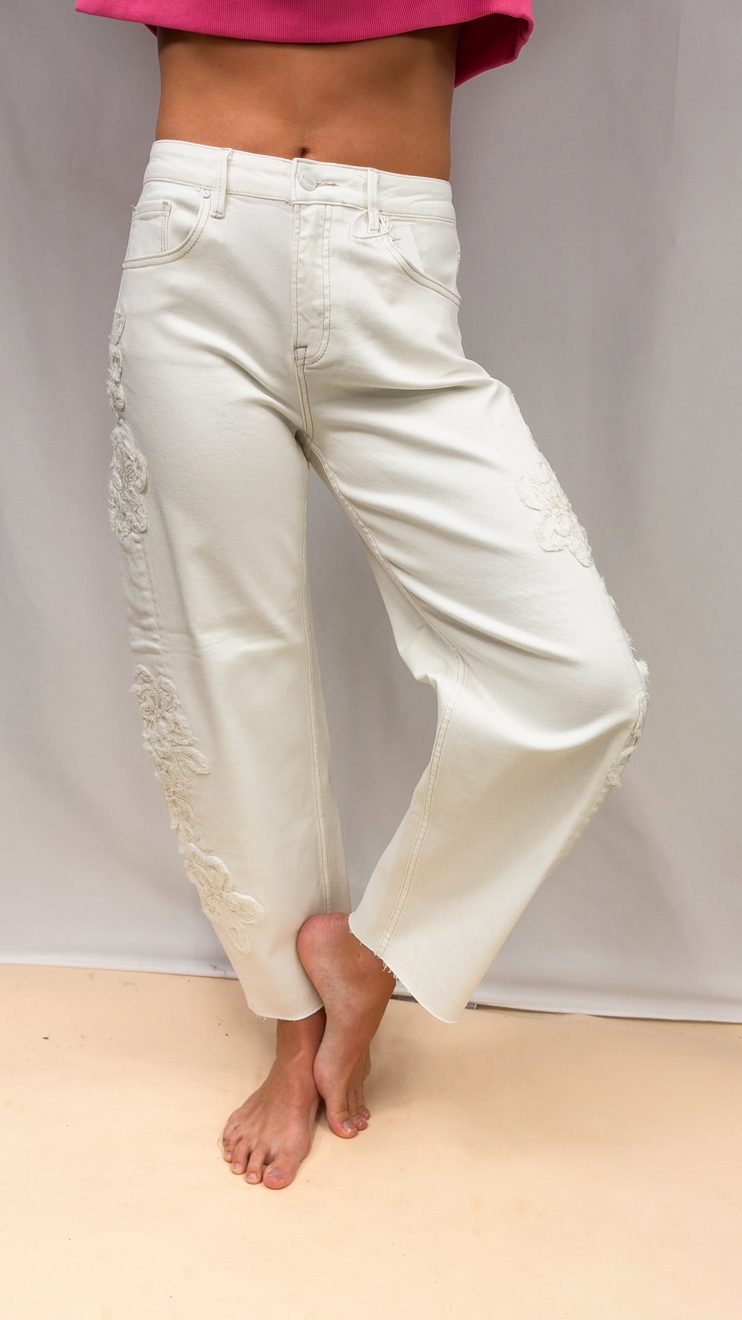 Woman wearing cream color jeans with flower appliques on plain background