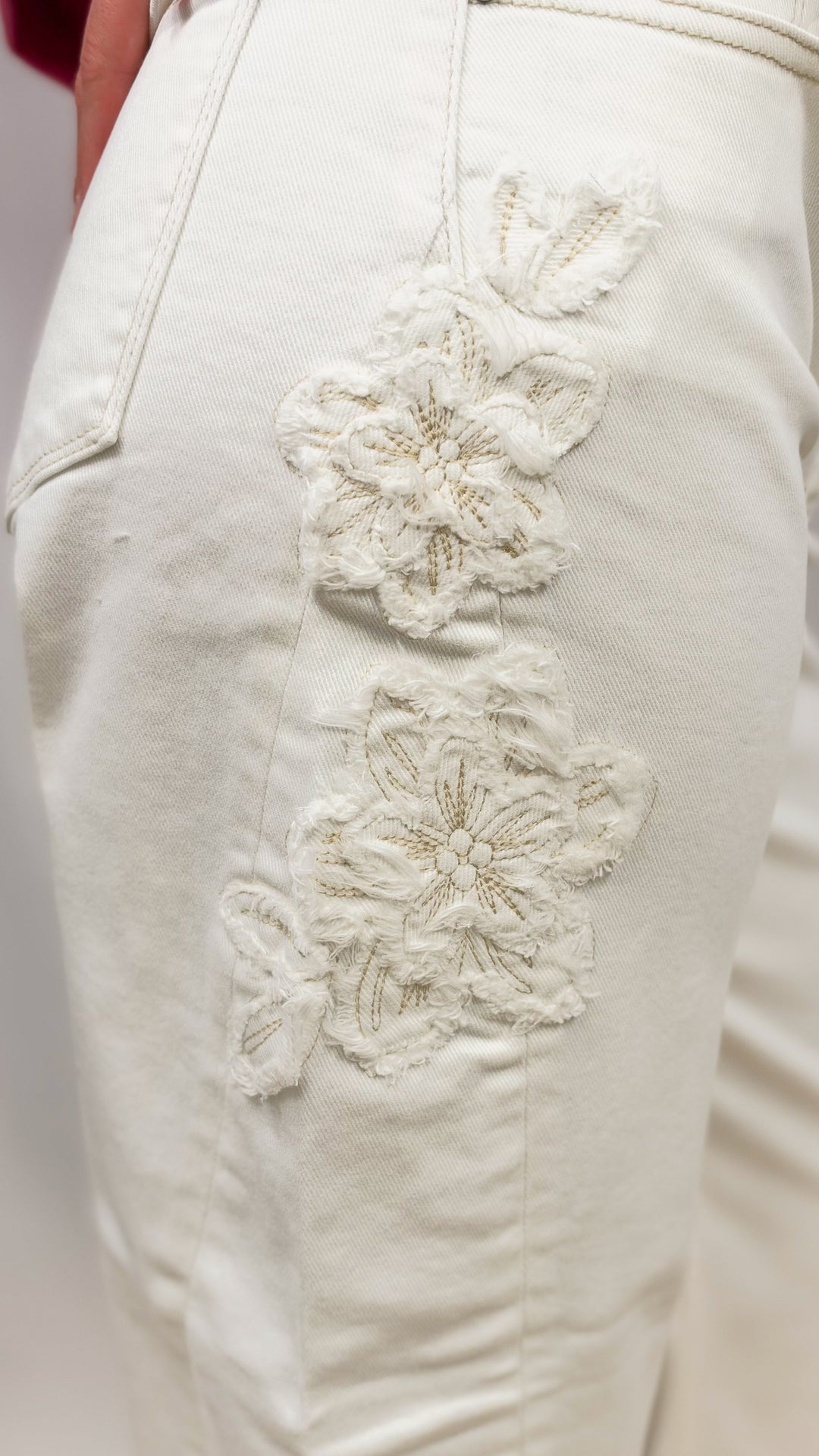 Woman wearing cream color pants showing up close detail shot of floral appliques on plain background