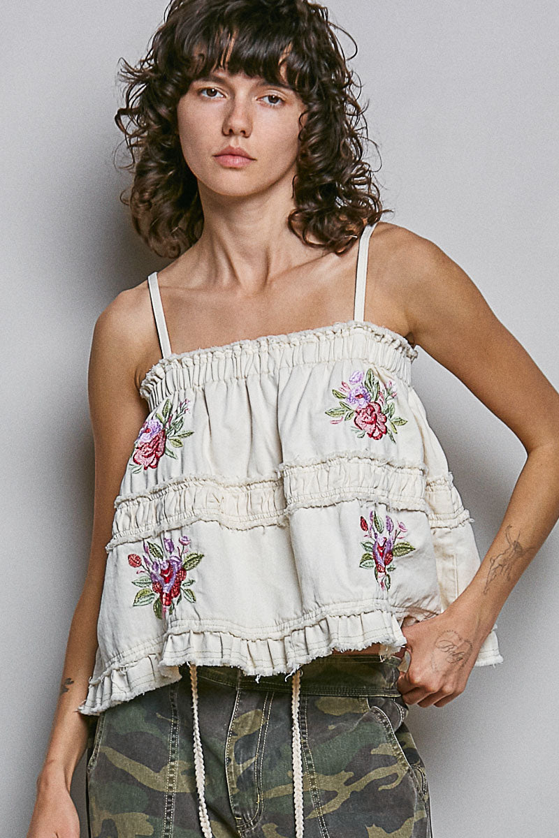 Woman wearing embroidered tank with camo pants on plain background