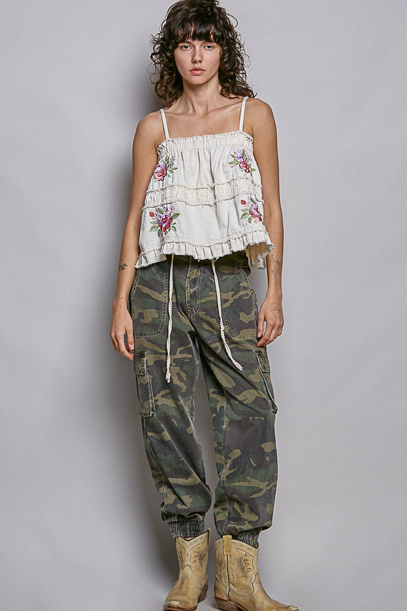 Woman wearing embroidered tank and camo pants on plain background