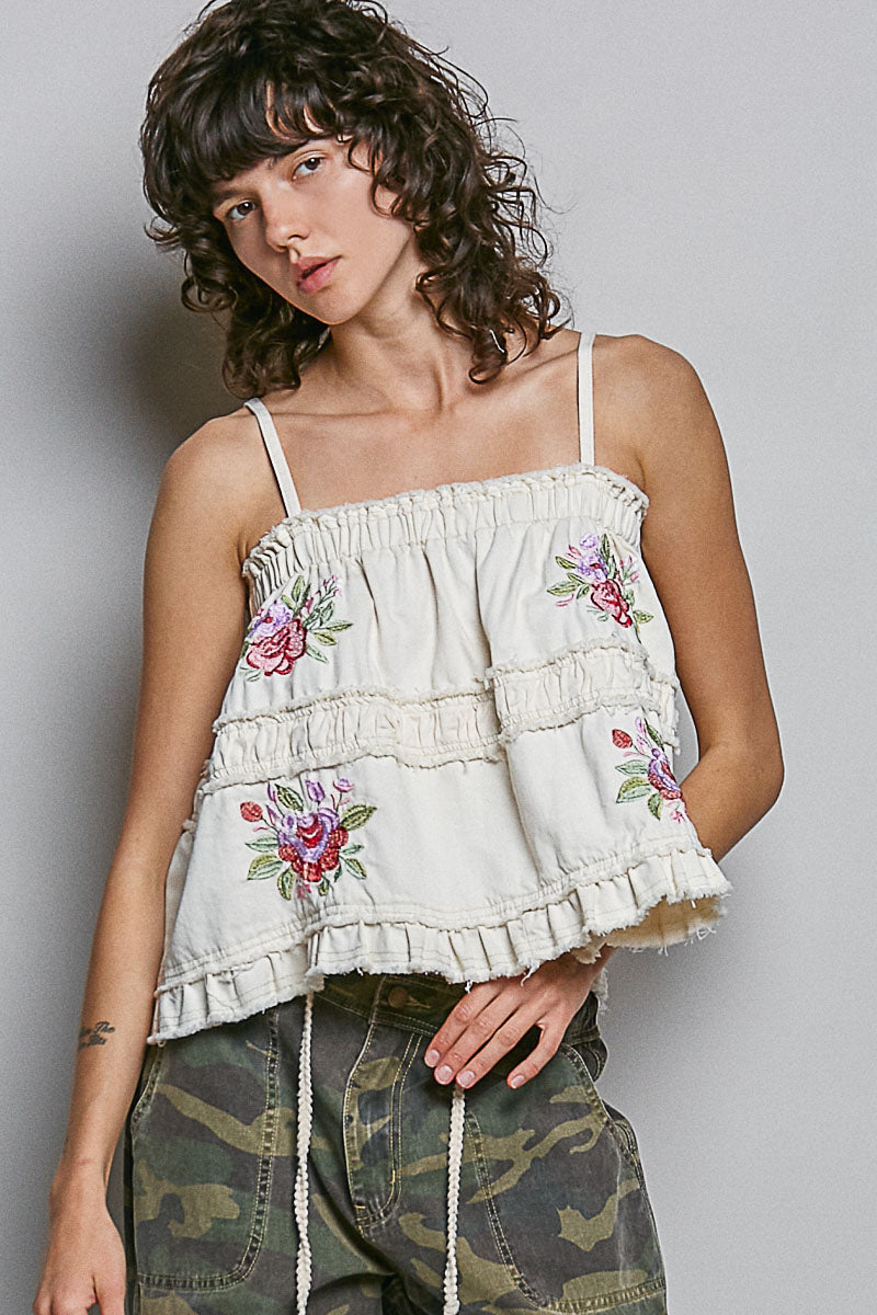 Woman wearing embroidered tank and camo pants on plain background