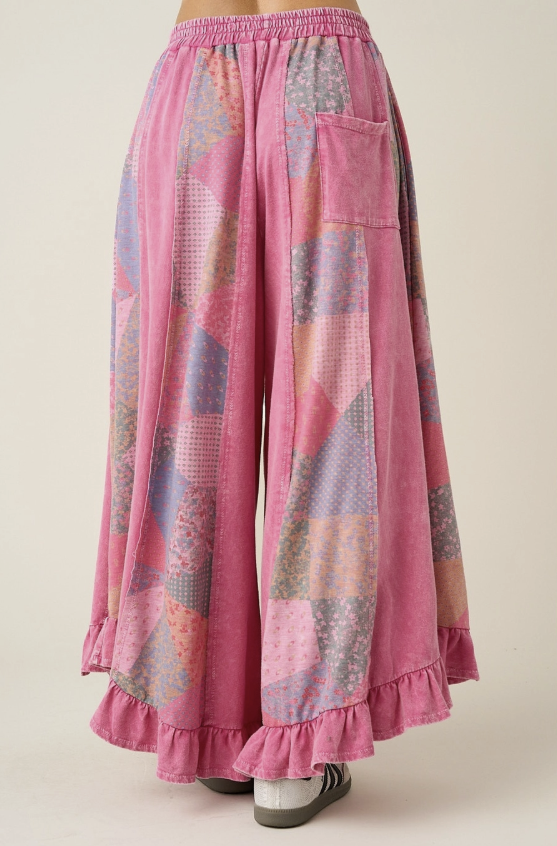Pink patchwork wide-leg pants with a ruffled hem and side pocket, shown on a model from the back against a light beige background.