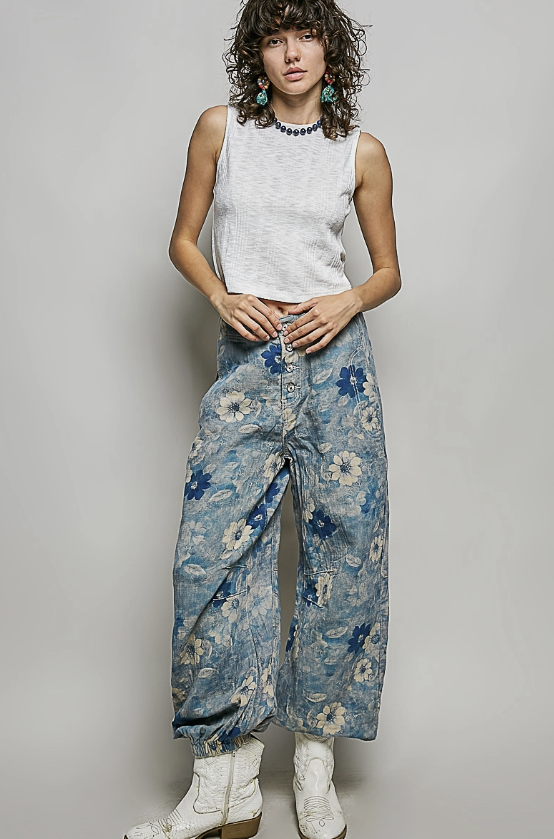 Woman wearing white tank and floral pattern pants on plain background