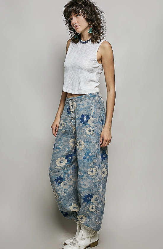 Woman wearing a white sleeveless top and floral blue pants against a plain background