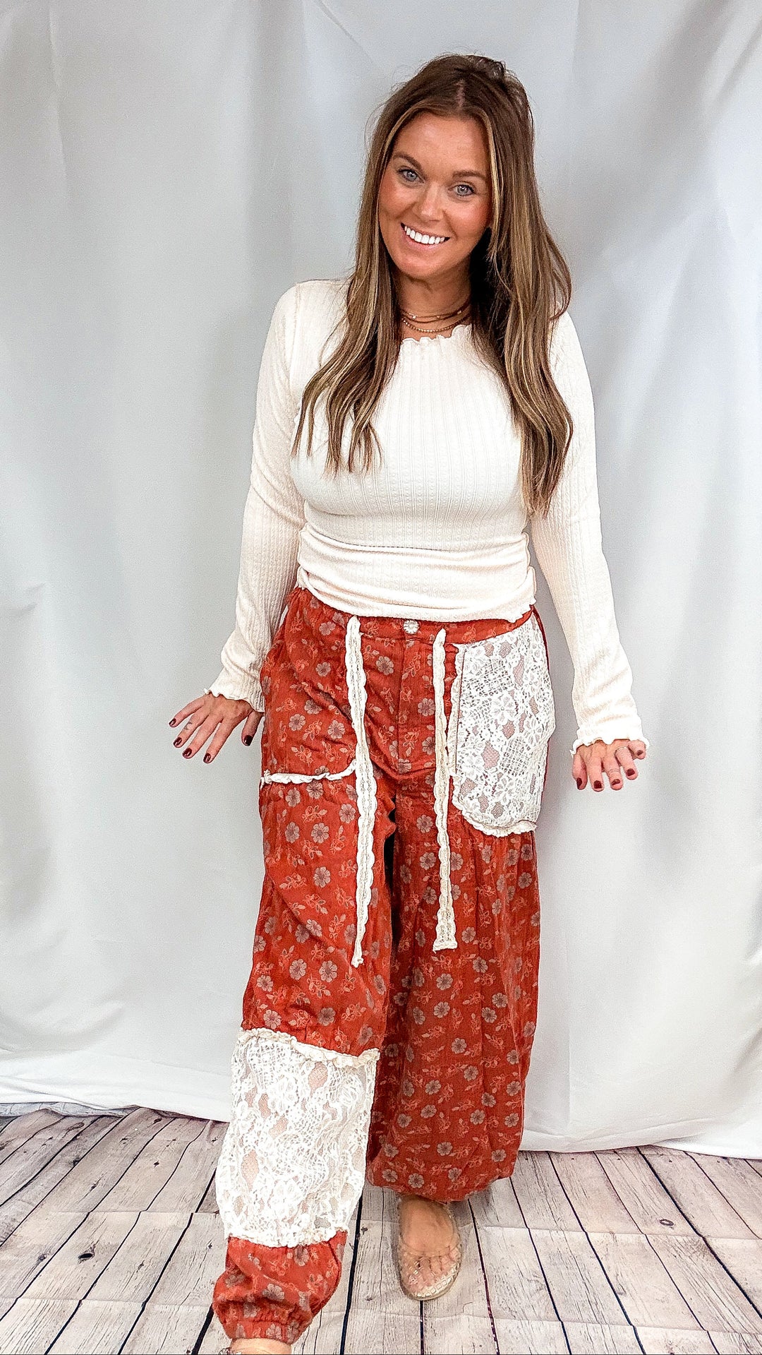 Woman wearing rust colored floral pants and cream top on plain background