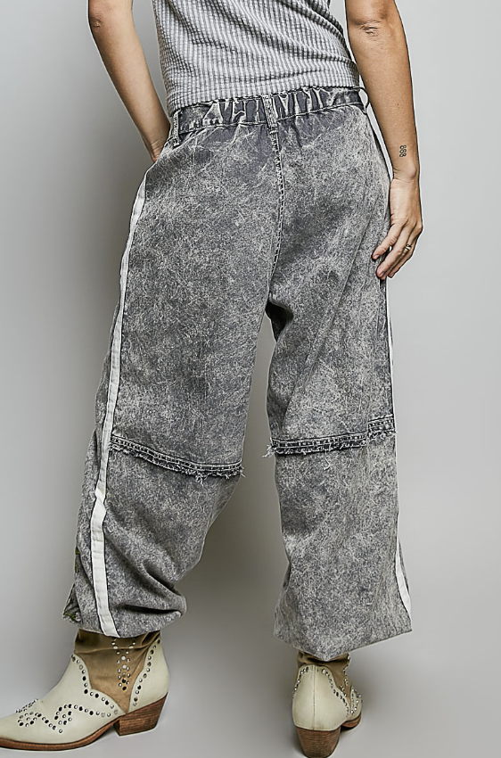 A person wearing wide-leg gray acid-wash pants with white side stripes, paired with a striped top and cream western-style boots, shown from the waist down against a light gray studio background.