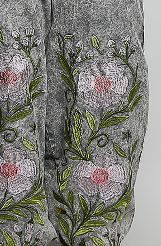 Close-up of gray fabric with embroidered floral pattern featuring white and pink flowers and green leaves.