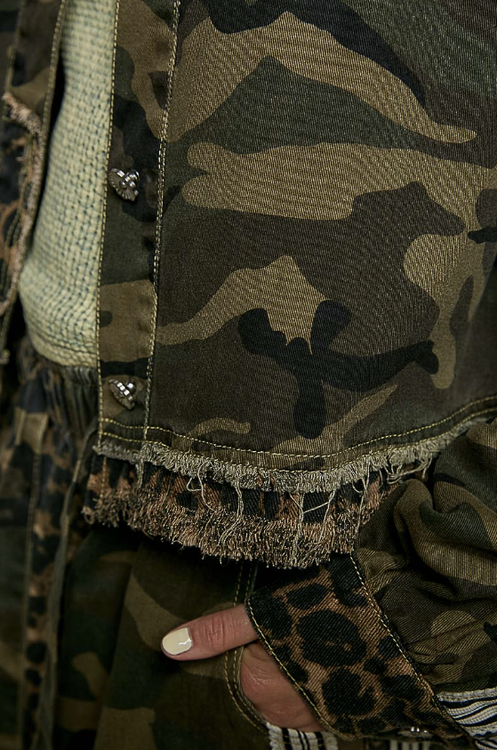 Close-up of a camouflage jacket with frayed hem, leopard-print fabric, and a hand with pale yellow nail polish tucked into a pocket.