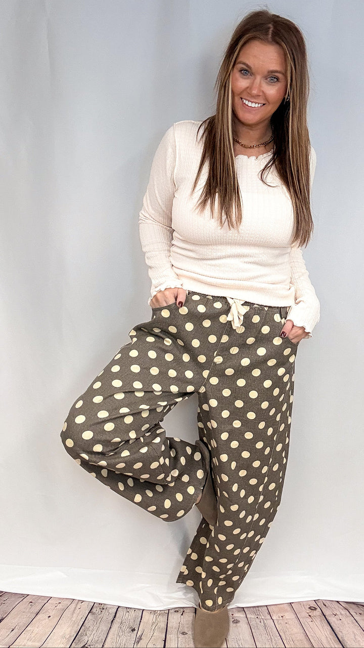 Woman wearing beige long sleeve top and grey polka dot pants on plain background