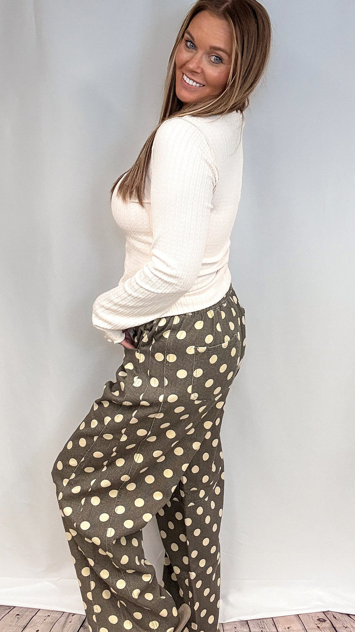 Woman wearing beige long sleeve top and grey polka dot pants on plain background
