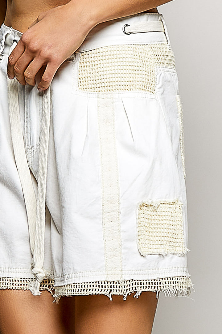 White denim shorts with frayed edges and a patch on a plain background