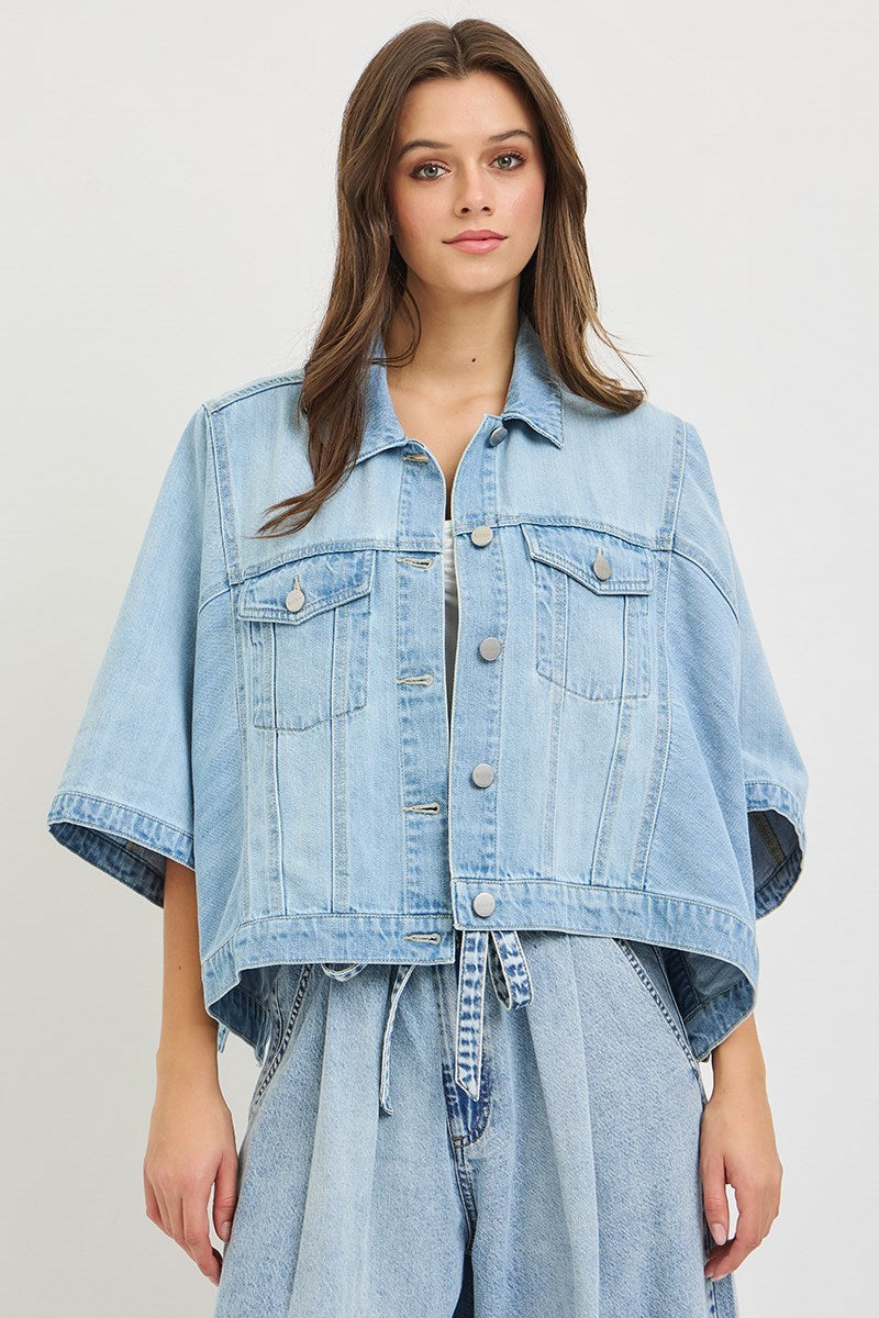 Woman wearing denim cape jacket on plain background