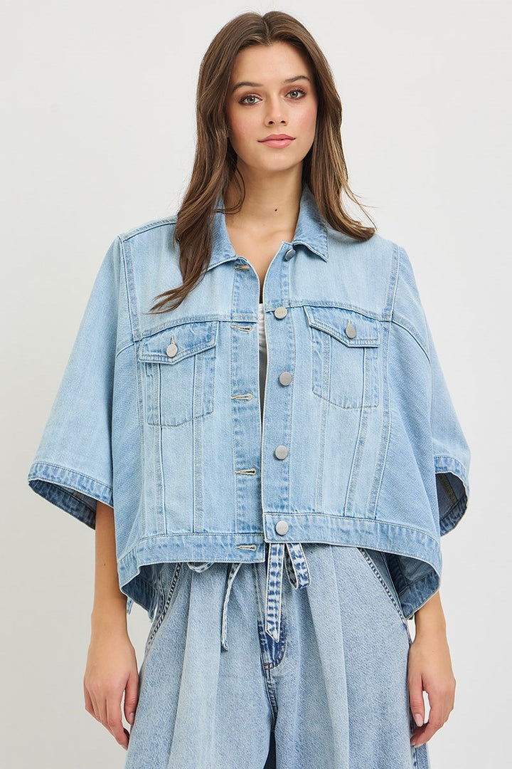 Woman wearing denim cape jacket on plain background