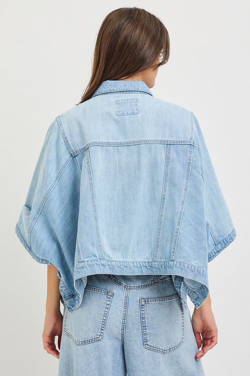 Back of woman wearing denim cape jacket on plain background