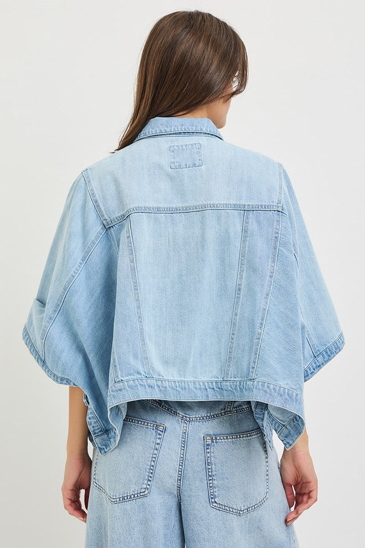 Back of woman wearing denim cape jacket on plain background