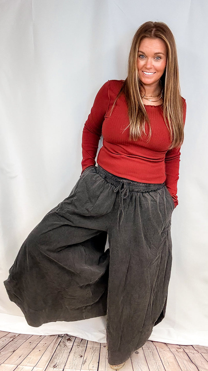 Woman wearing black pants and red long sleeve shirt on plain background