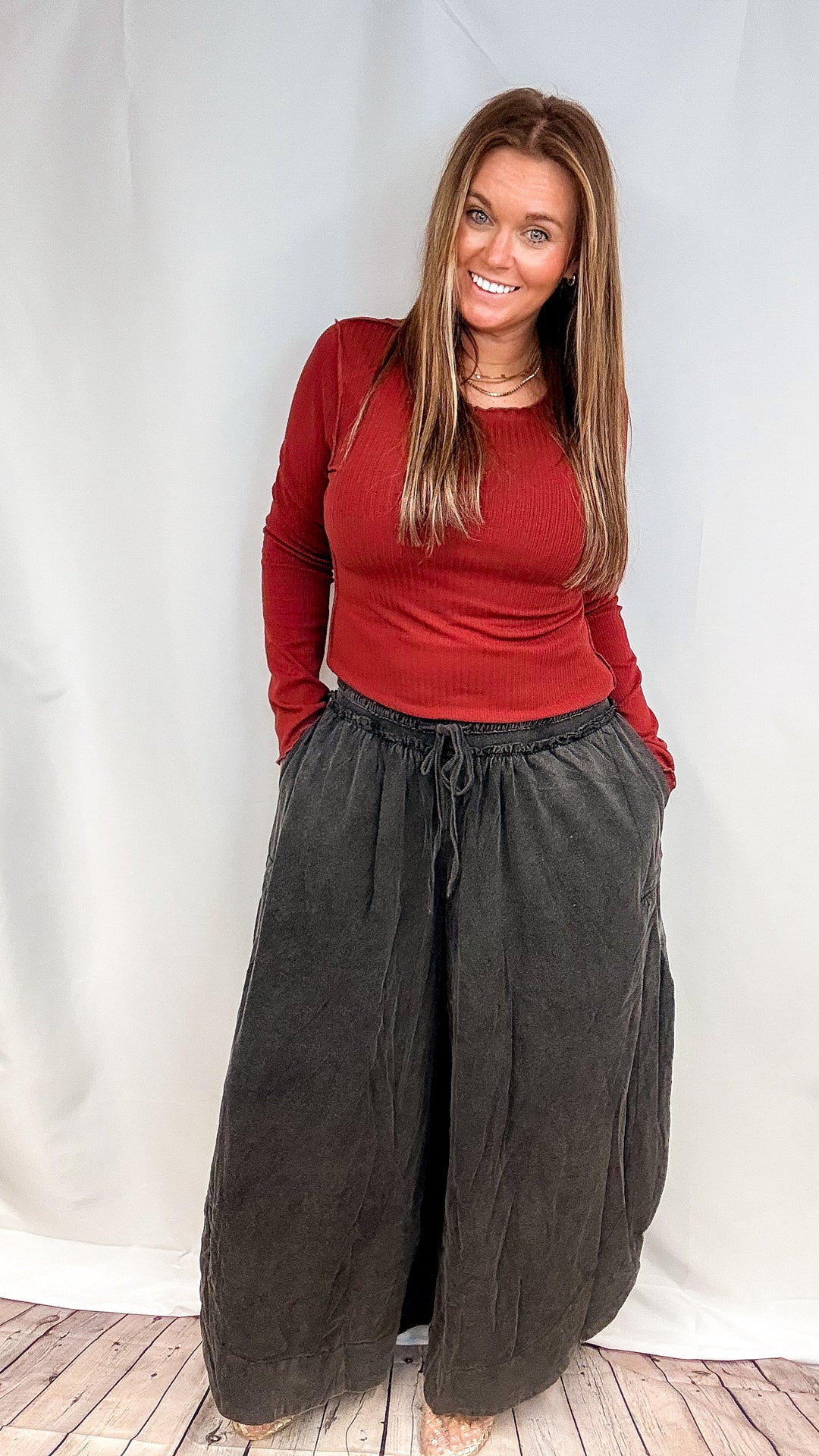 Woman wearing red long sleeve top and black pants on plain background