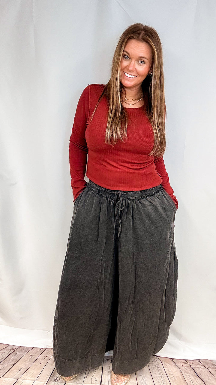 Woman wearing red long sleeve top and black pants on plain background