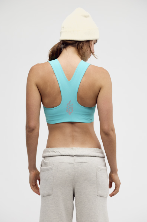 Person wearing a turquoise sports bra and gray sweatpants on a white background