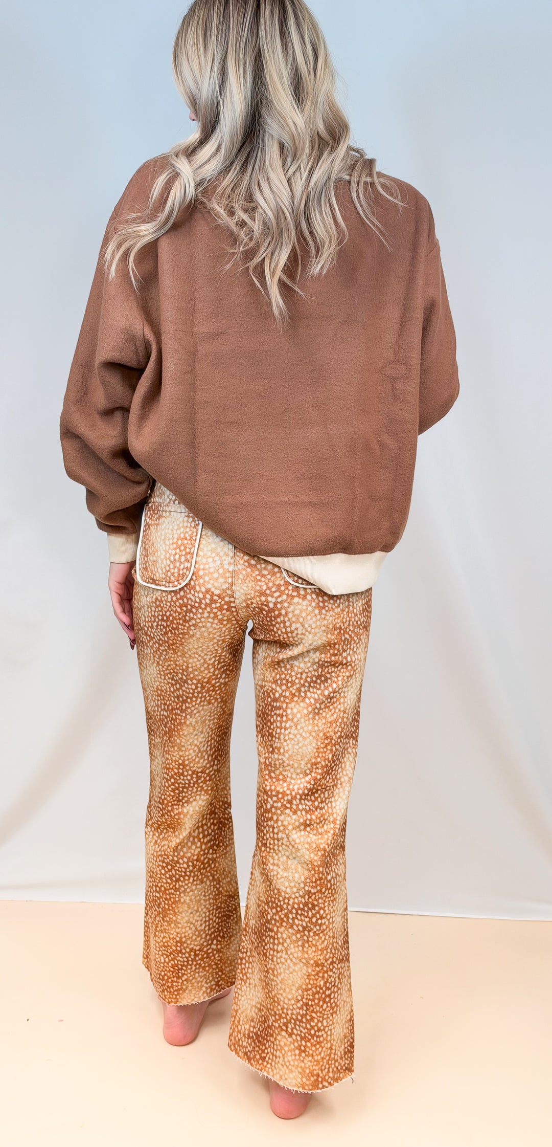 Woman shown from back view wearing brown sweatshirt with fawn print pants on plain background