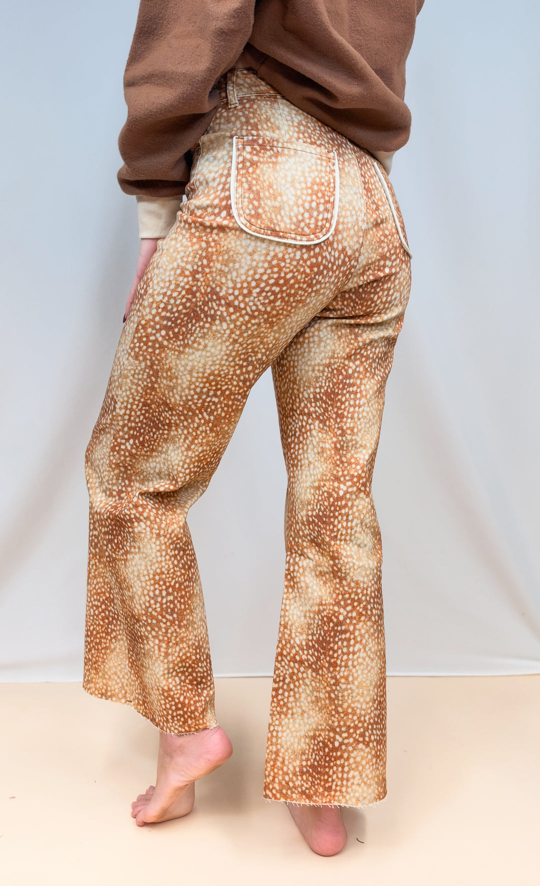 Woman shown from back view waist down wearing fawn print pants on plain background