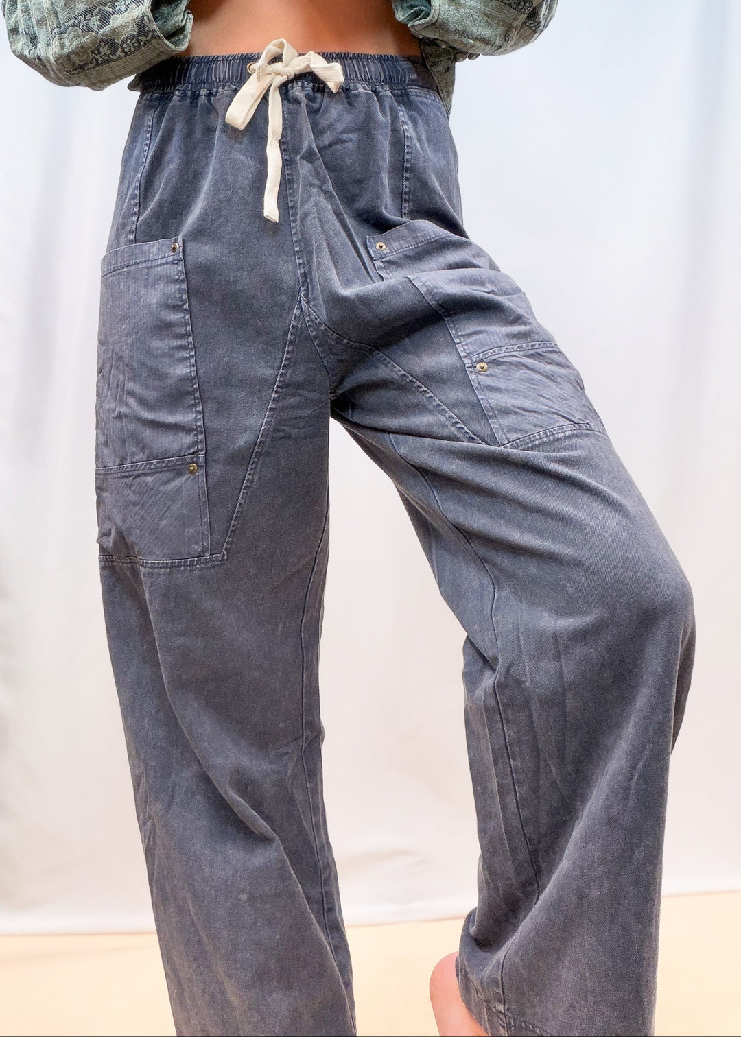 Woman shown from waist down wearing blue twill pants with large front pockets on plain background