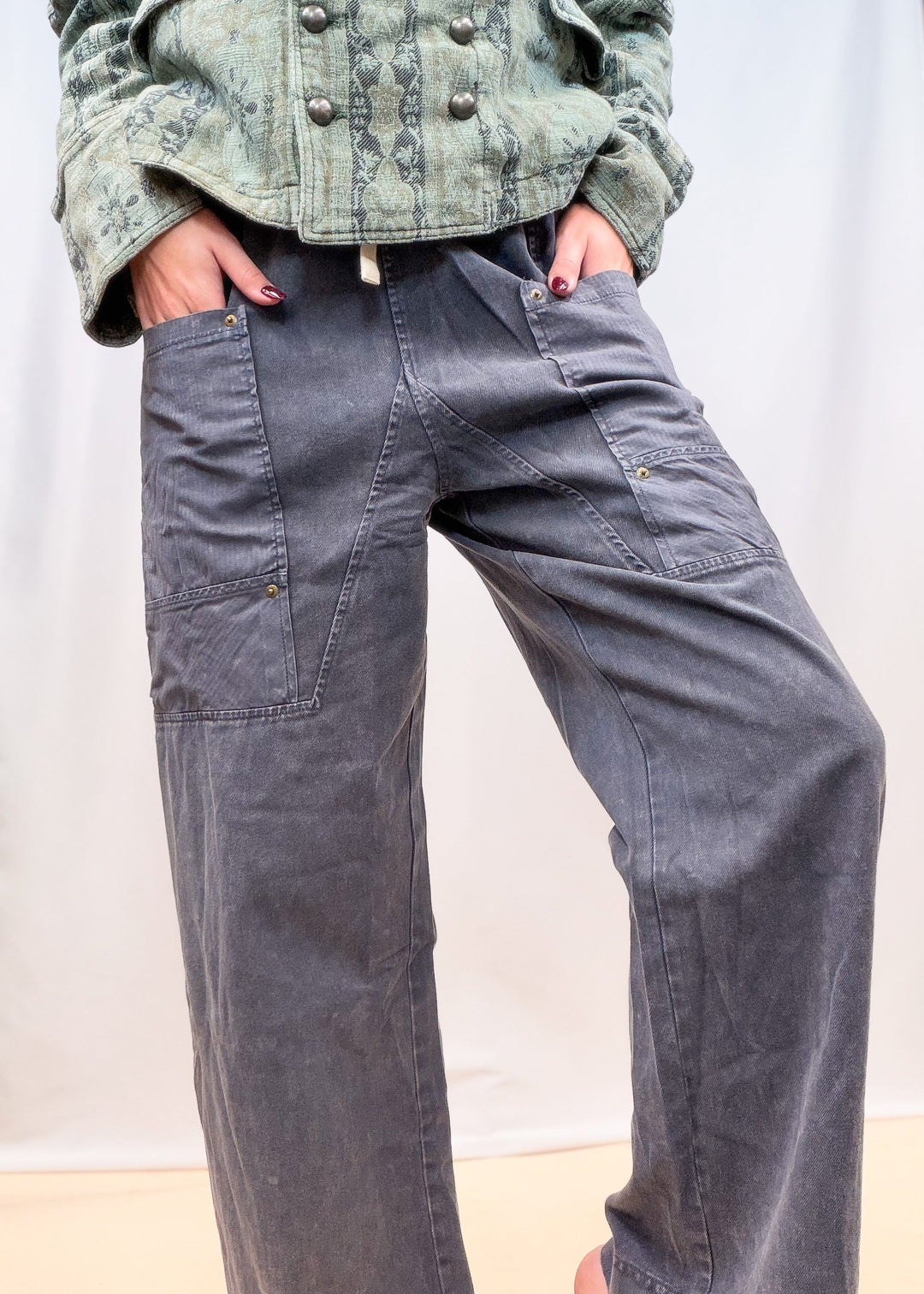 Woman shown from waist down wearing blue twill pants with large front pockets on plain background