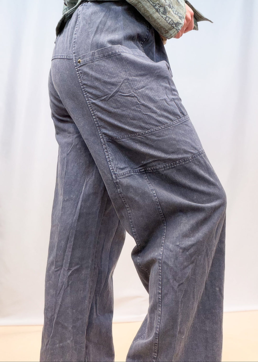 Woman shown from side view wearing blue twill pants on plain background