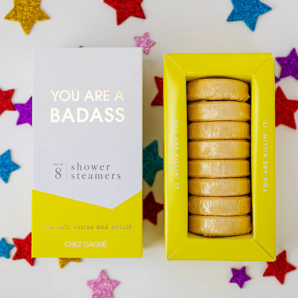 A boxed set of shower steams from Chez Gagnée, shown with the outer box on the left and the yellow tray containing eight wrapped steams on the right. The packaging is white and yellow with the text &