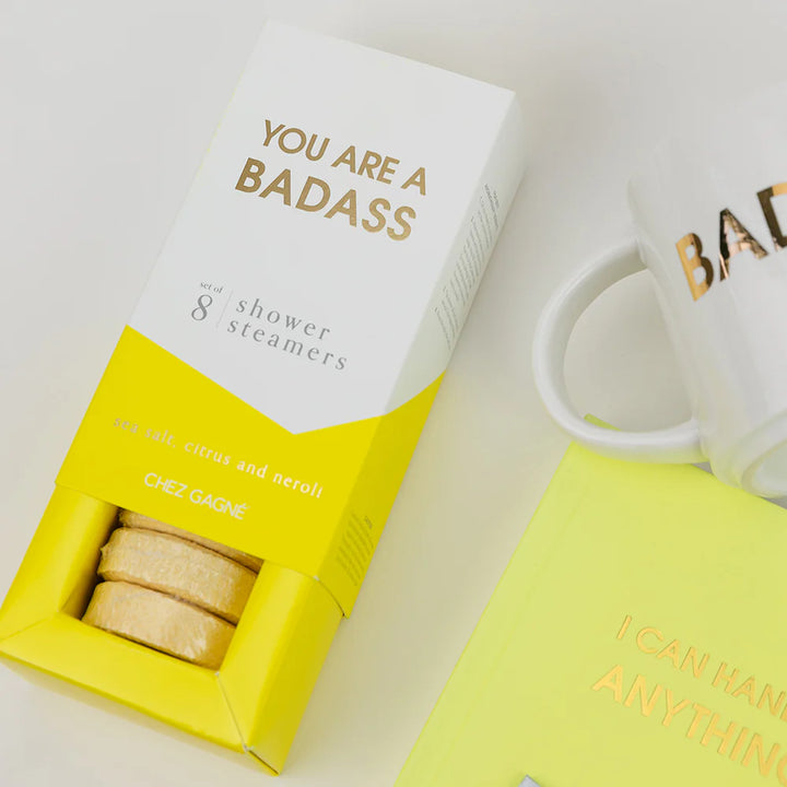 Chez Gane shower steamers in a white and yellow box with gold foil text, styled on a light background next to a white mug and a neon yellow card.