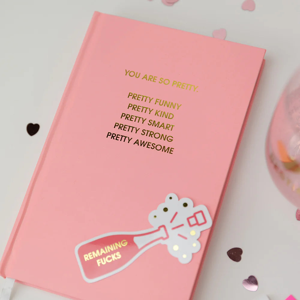 Pink notebook with motivational text and a sticker on a light background