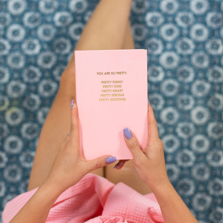 Person holding a pink book with motivational text against a blue patterned background