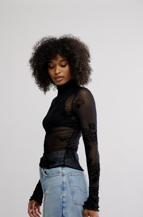 Woman wearing black mesh floral top with blue jeans on white background