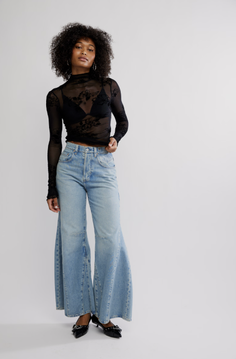 Woman wearing black mesh floral top with blue jeans on white background