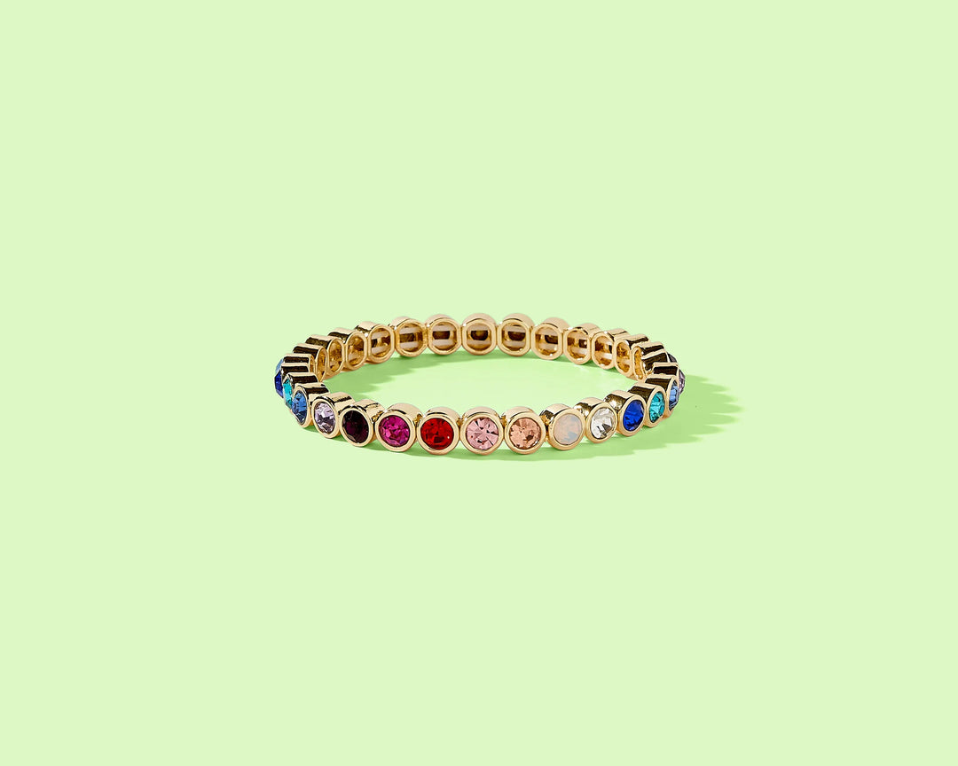 Gold bracelet with colorful gemstones on a light green background